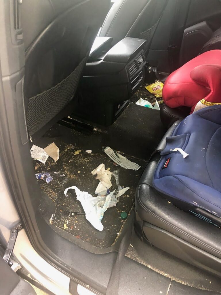 Family SUV back seat floor covered in trash and crumbs before an interior car detail in San Diego